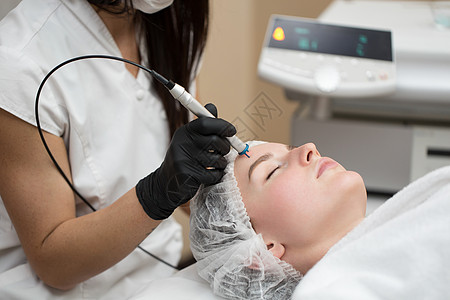 治疗师美容师在美容 SPA 诊所对年轻女性的脸进行激光治疗 激光去除皮肤血管的特写过程身体护理脱毛化妆品沙龙女孩机器仪器电解剃须图片