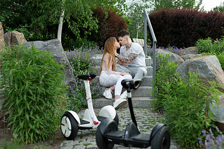 年轻男人和女人在公园里亲吻 在前方的悬浮板上青年摩托车人行道木板电池男性车辆女孩车轮电气图片