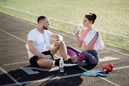 夏天在体育场跑步后 男人和女人坐在运动机上 他们用耳机听音乐图片