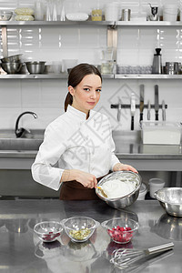 可爱的年轻女性面包师在大碗里混着面团和微笑 做蛋糕或蛋糕的过程图片