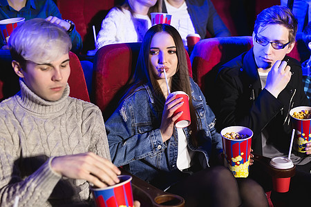 欢快的公司在电影院 一个女孩从玻璃杯里喝水 一个男人吃爆米花图片