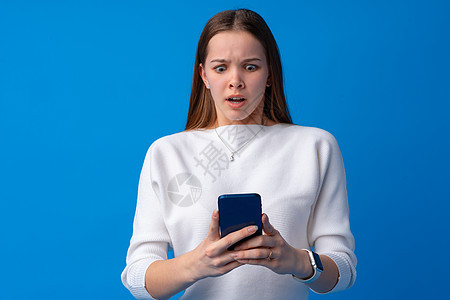 蓝色背景下使用智能手机的少女肖像女士女孩衣服女性视频技术快乐阅读细胞休闲装图片
