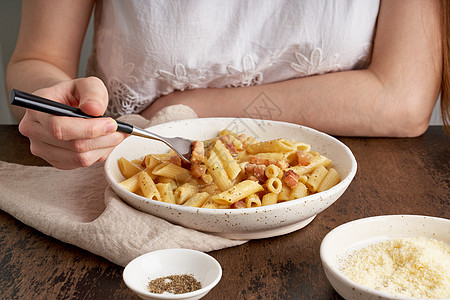 女人坐在桌边吃着意大利面和潘斯塔肉饼食物奶油香料美食食谱火腿熏肉女性猪肉胡椒图片