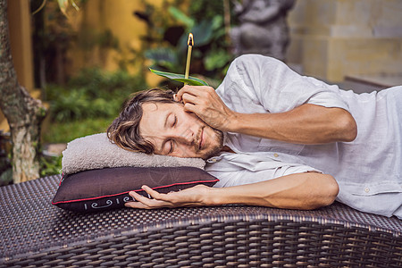 在热带花园的背景下进行耳烛疗法的男士图片