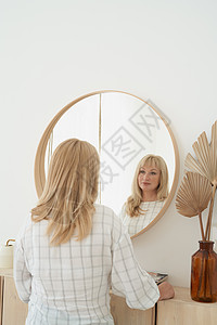 中年妇女看着自己 长头发的美丽金发美女仰慕着她自己的反光浴室反射长发思考女性圆圈镜子图片