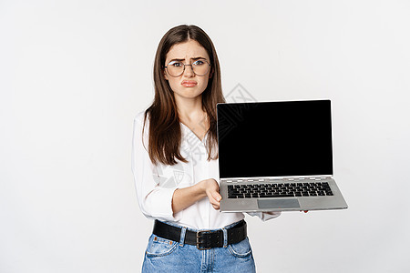 悲伤的黑发女孩 展示笔记本电脑屏幕的学生和惊心动魄的沮丧 在白人背景面前感到失望图片