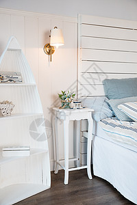 斯堪的纳维亚风格的明亮舒适的卧室室内设计 床头柜上的鲜花 在床上装饰房间内部的枕头 桌子上方燃烧着小灯图片
