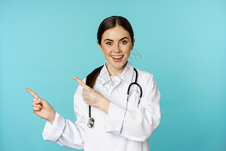 微笑的医务工作者的画像 穿白大衣的女医生拿着听诊器 手指向左 展示医疗诊所广告 绿松石背景护士横幅蓝色女士成人职员女孩药品工作室图片