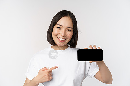 车站显示屏微笑的韩国女性用手指指着手机屏幕的肖像 显示水平智能手机显示屏 推荐网站或在线商店 白色背景企业家细胞女士成人购物情绪互联网技术背景