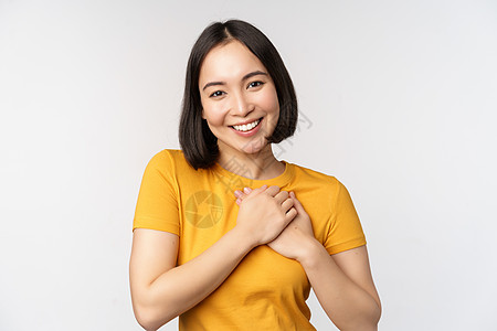 浪漫的亚裔女性朋友 握着手在心上 带着关爱和温柔微笑 穿着黄色T恤站在白色背景之上压痛商业大学互联网成人学生购物女士工作室技术图片