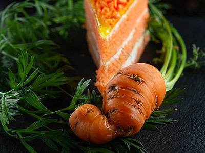 一块胡萝卜蛋糕放在石板上 一个长着绿叶的丑陋的新鲜胡萝卜四处走动背景