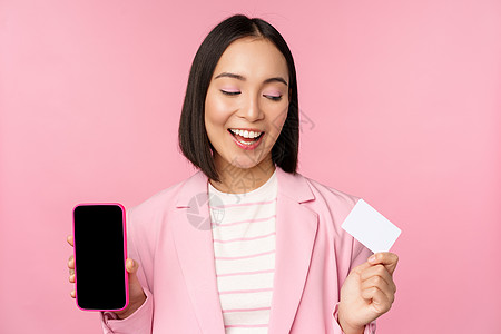 亲吻韩国女商务人士 展示移动电话屏幕 信用卡 在线银行应用程序界面 粉红背景等信息 单位 千分之一工作卡片购物标识命令商业经理售图片