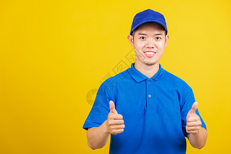 身穿蓝色T恤衫和帽子制服微笑 手举大拇拇指的手势经销商男性衬衫商业职业员工工作室手指相机运输图片