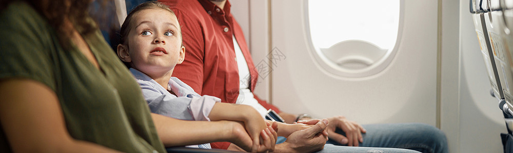 喜悦的caucasians家庭 父母与小女儿在飞机上坐着时手牵手背景