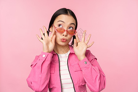 穿着时尚太阳镜的漂亮亚洲女性模特 装扮成粉红色背景 打扮成潮流服装 复制空间购物商业企业家微笑女朋友女孩快乐大学工作标识背景图片