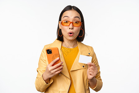 网上购物 戴着太阳镜 拿着信用卡和手机 微笑着开心 站在白色背景上的时尚亚洲女模特技术购物电话工作促销情感企业家卡片成人商业背景图片