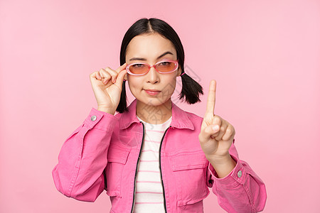 照片来自亚洲女孩的严肃面孔 显示禁止 责骂手势 摇动手指举起 表示不赞成 站在粉红背景上情绪商业广告购物情感手指学生女朋友办公室图片