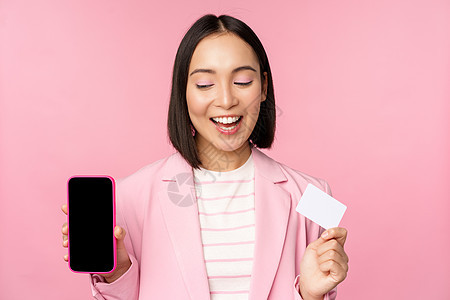 亲吻韩国女商务人士 展示移动电话屏幕 信用卡 在线银行应用程序界面 粉红背景等信息 单位 千分之一工作职场工作室经理广告售货员成图片