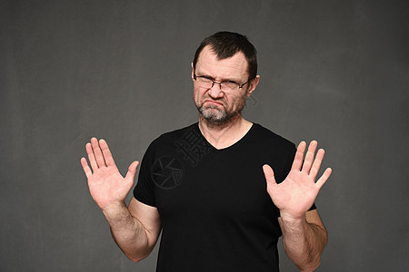 穿黑色T恤带眼镜的成人男子 手放在灰色背景上 举起手来图片