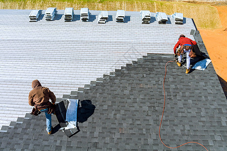 工人用手安装沥青屋顶 用气锤和钉子打刺图片