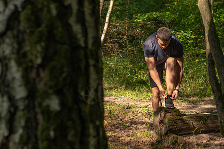 这位运动员正在用运动鞋系住他腿上的鞋带 运动员在户外的公园里跑步 在森林周围 橡树绿草年轻持久的运动员活跃的跑步者森林 锻炼慢跑图片