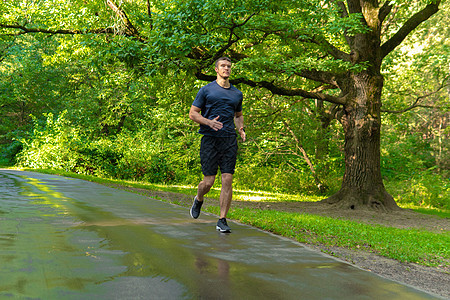 一名男子运动员在户外公园跑步 在森林周围 橡树绿草年轻持久的运动员跑步运动 户外耐力人慢跑健康 夏季能量交叉 双脚伸展图片