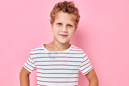 穿条纹T恤T恤粉色颜色背景的卷发男孩图片