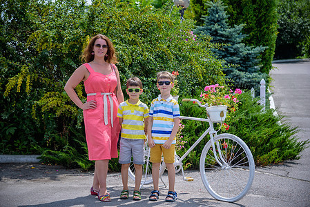 孩子们站在温暖的阳光天气下 与家人共度闲暇时光 在自行车旁有鲜花的双胞胎和两个男孩乐趣娱乐孩子微笑儿子活动成人骑术男生母亲图片
