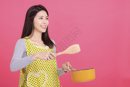 快乐的年轻女家庭主妇在做饭时穿着厨房厨师微笑围裙烹饪平底锅乐趣女性家务食物油炸图片
