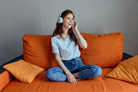 坐在沙发上坐在家里听耳机技术音乐的女睡在沙发上乐趣微笑女性女孩闲暇喜悦客厅黑发房间快乐图片
