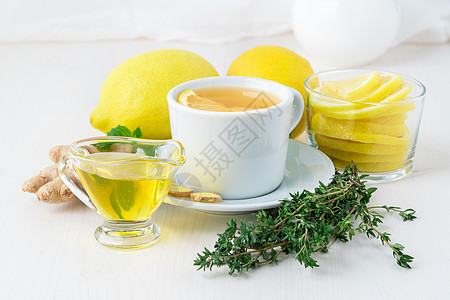 民间流行的治疗感冒的方法 — 一杯茶和一片柠檬 生姜 薄荷 蜂蜜 香草 整个柠檬和一半的白色背景 侧视图图片