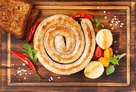 土制炸烤香肠 螺旋形状 蔬菜和面包在黑木切削板上 顶视角图片