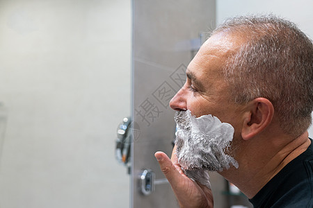 英俊帅气的男子将剃须泡沫涂在脸上 用剃刀割掉胡子和胡子刮胡子成人中年男性凝胶镜子皮肤胡须奶油护理图片