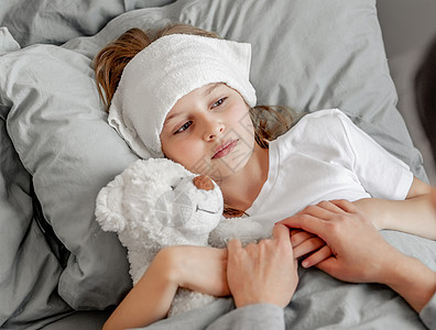 床上有泰迪熊玩具的女童女孩睡衣枕头压缩拥抱父母母亲童年就寝毯子时间图片