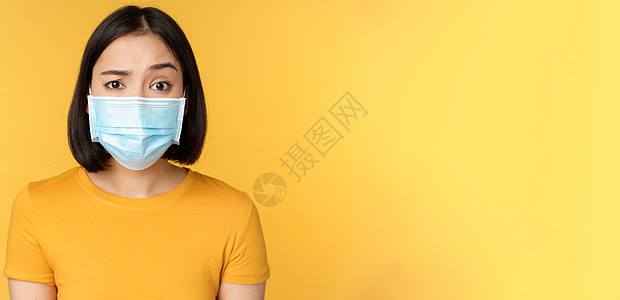 蒙上医疗面罩 引起眉眉怀疑 站在黄色背景之上的持怀疑态度和困惑的亚洲妇女肖像女士互联网情绪购物成人女孩工作室技术健康学生图片