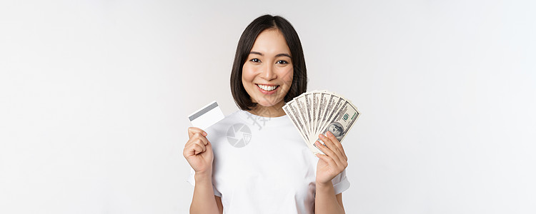 手持信用卡和现金 美元 身穿白衣穿着短衫站在白底背面上 这简直是一幅亚洲女人微笑的肖像女孩情感商业互联网成人学生女士银行女性横幅图片
