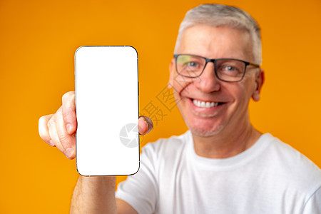 长得帅的笑着微笑的高级男子拿着智能手机 在黄色背景上显示屏幕绅士电话喜悦空白快乐眼镜退休手指祖父成人图片