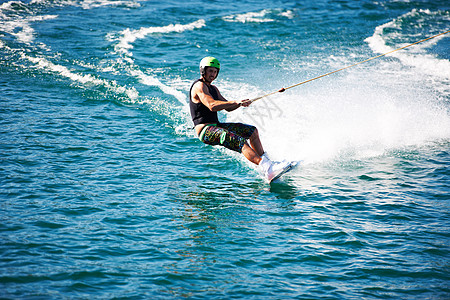 一个戴着头盔和救生衣的年轻人在湖上滑水 一个戴着头盔和救生衣的年轻人在湖上滑水绳索娱乐滑雪太阳木板海洋训练阳光成人闲暇图片