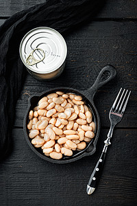 白肾豆 带有金属罐头的白肾豆 在铁煎锅中 在黑木制桌子背景上 顶层视野平铺图片