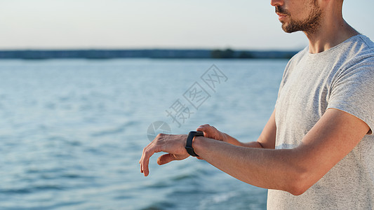 运动男子与聪明的健身手表站在海岸上图片