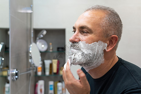 英俊帅气的男子将剃须泡沫涂在脸上 用剃刀割掉胡子和胡子凝胶中年隔断男性奶油头发皮肤镜子浴室护理图片