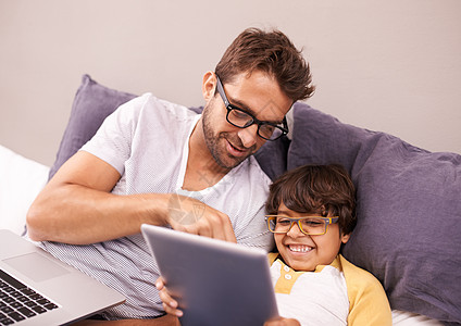 父亲和儿子躺在床上 同时使用笔记本电脑和数字平板电脑图片