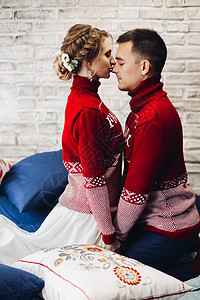 红色圣诞跳跃者的情侣 在枕头周围亲吻编织压痛幸福婚礼眼睛夫妻发型丈夫砖墙未婚夫背景图片