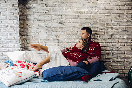 红色圣诞跳跃者的情侣 在枕头周围亲吻婚姻妻子新年压痛夫妻毛衣编织新郎发型未婚夫背景图片