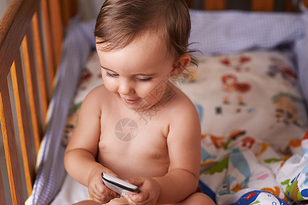 她对手机很着迷 有个小女孩坐在婴儿床里玩她的手机 她喜欢听手机图片