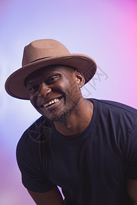 笑笑快乐的美国非洲男人穿着时髦的帽子 在粉色和紫色背景上穿庆典男性派对微笑成人黑色冒充情感拳头工作室图片
