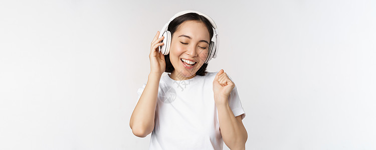 现代的亚洲女孩舞蹈 用耳机听音乐 笑笑快乐 站在白色背景的T恤衫上广告情感工作室情绪大学女朋友女士互联网横幅购物图片