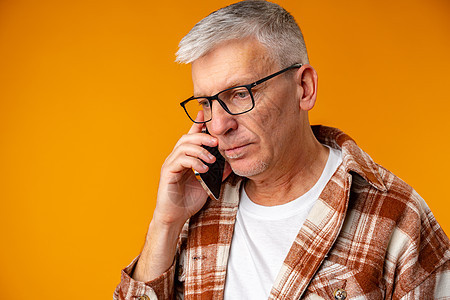 悲哀的欧洲老人在黄色背景下通过电话交谈的肖像退休老年手机父亲祖父讲话休闲装长老细胞技术图片