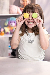 用蛋白杏仁饼干捂住眼睛的小女孩开心的笑脸 十几岁的女孩玩甜点马卡龙 把饼干像眼镜一样放在眼睛周围 把手扔到两边图片