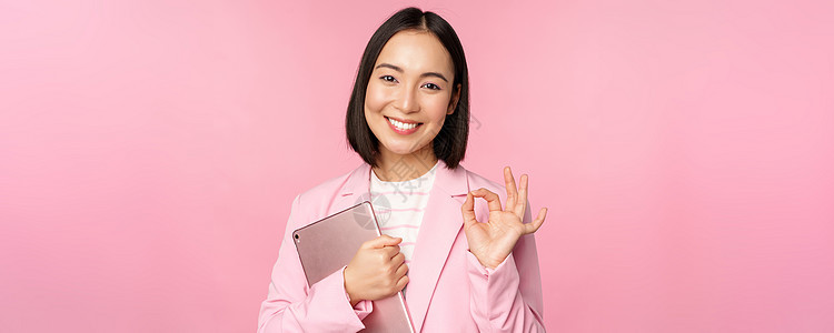 公司女性的肖像 身穿商业西装 持有数字平板牌 表现好 推荐公司 站在粉红背景之上的女同事经理工作标识职场人士办公室黑发工作室企业图片